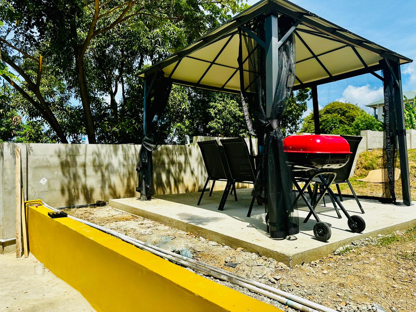 Outdoor shaded dining area at Seaview Escape Tobago with barbecue grill, surrounded by lush greenery.